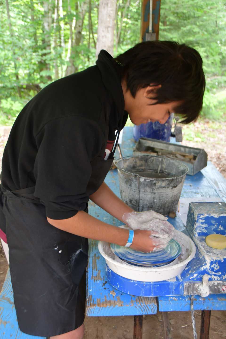 A scout leans over a pottery tool, working on his pot