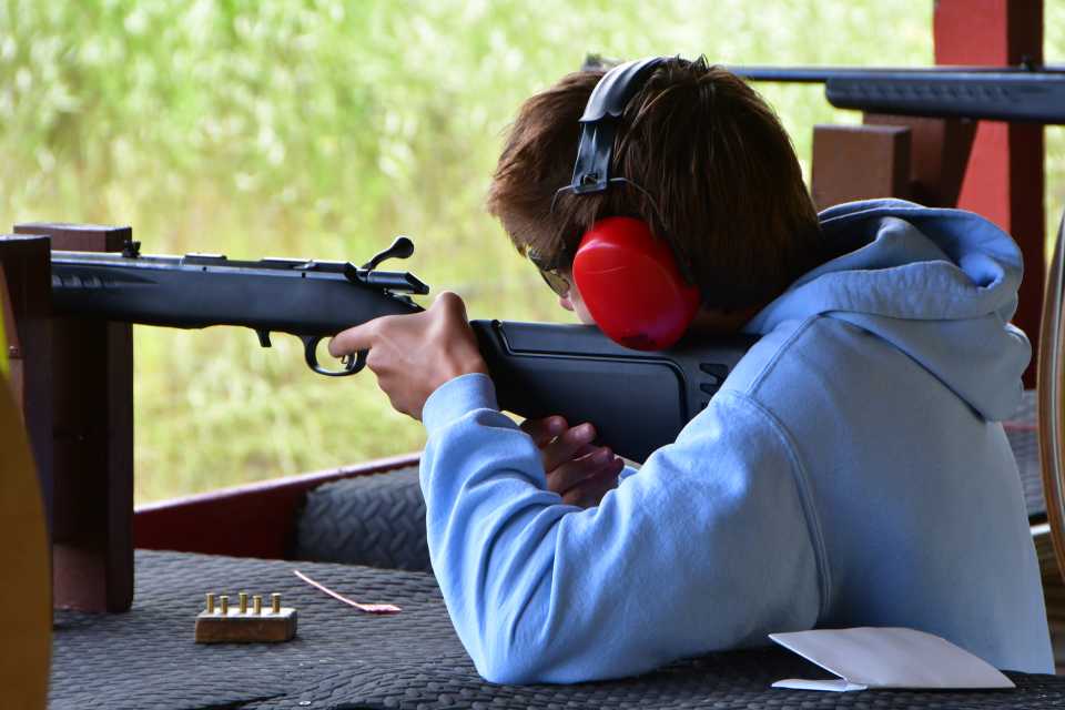 A boy aims carefully down a rifle sight, wearing ear protection