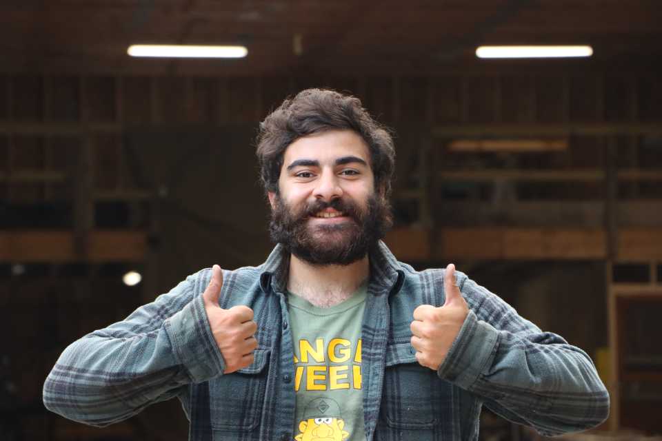 A bearded man looks at the camera with and gives two thumbs-up gestures with a grin